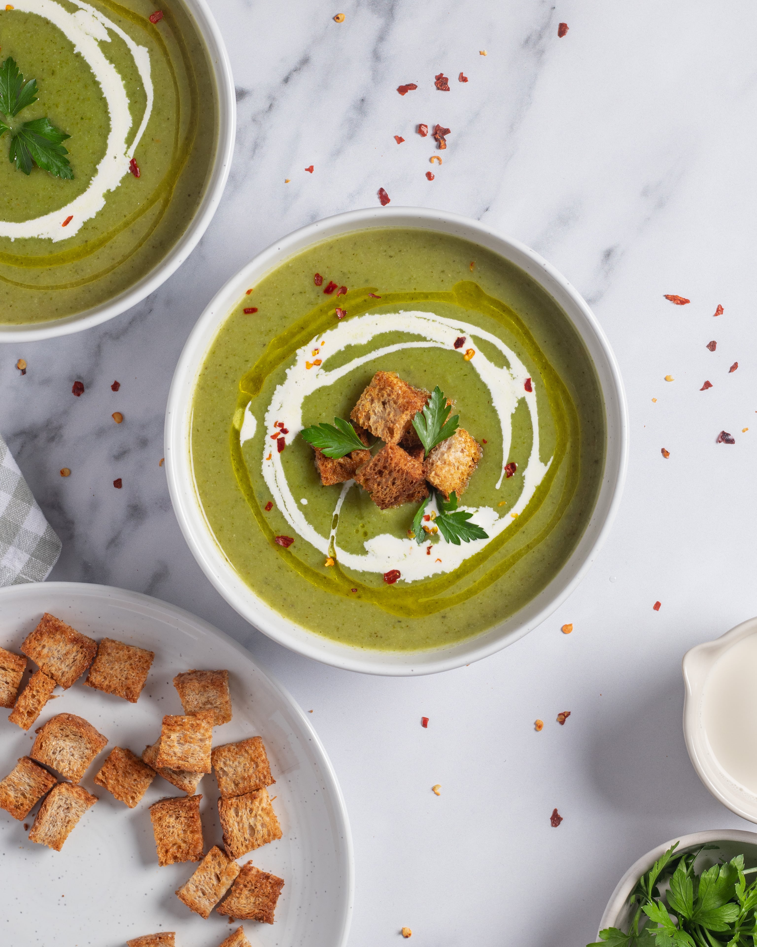 Overhead shot of creamy green vegetable soup with croutons and cream swirl